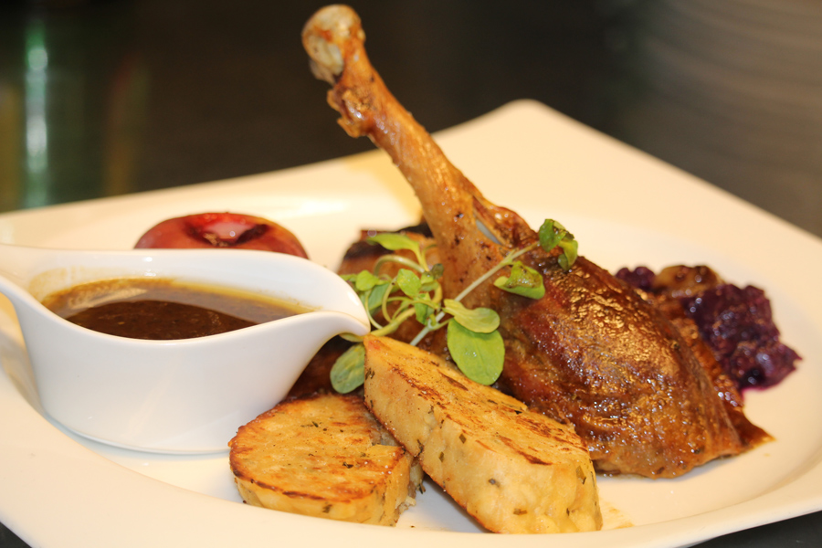 Ein gebratenes Gansl mit Serviettenknödel und Sauce auf einem weißen Teller